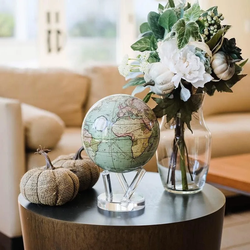 Globe Mova Antique Cassini vert posé sur une table basse avec des fleurs