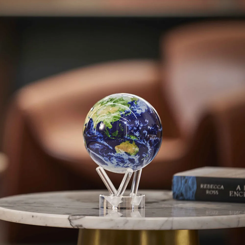 Globe Mova Terre avec nuages posé sur un support transparent, sur une table en marbre dans un salon